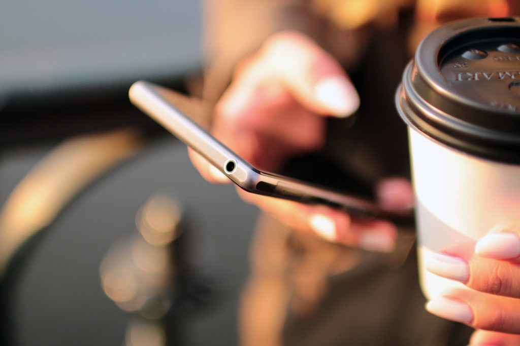 Person holding their smartphone and a cup of coffee